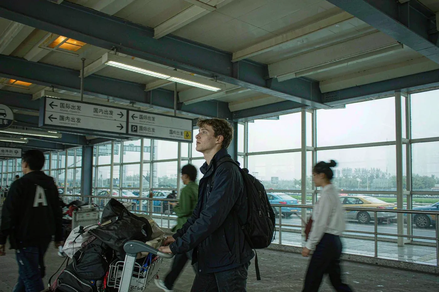 A foreign traveller with a luggage trolley looking at signs in a Chinese airport arrivals hall