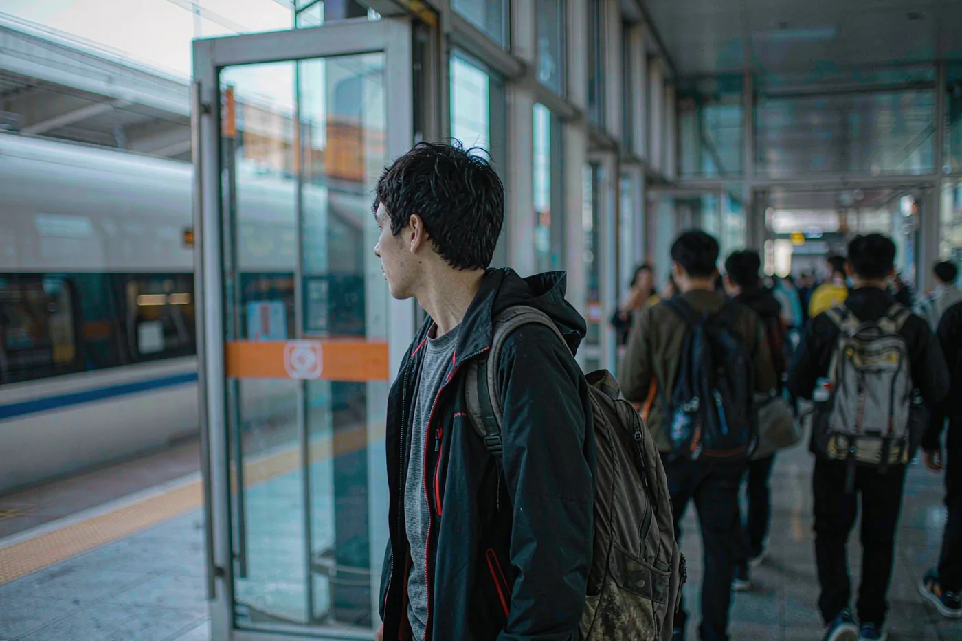 A foreign traveller with a backpack watching a high-speed train at a Chinese railway station