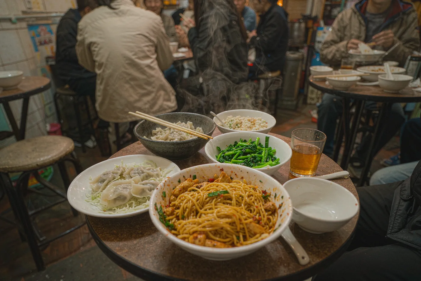 Shared dishes of noodles, dumplings and greens on a table in a casual Chinese restaurant