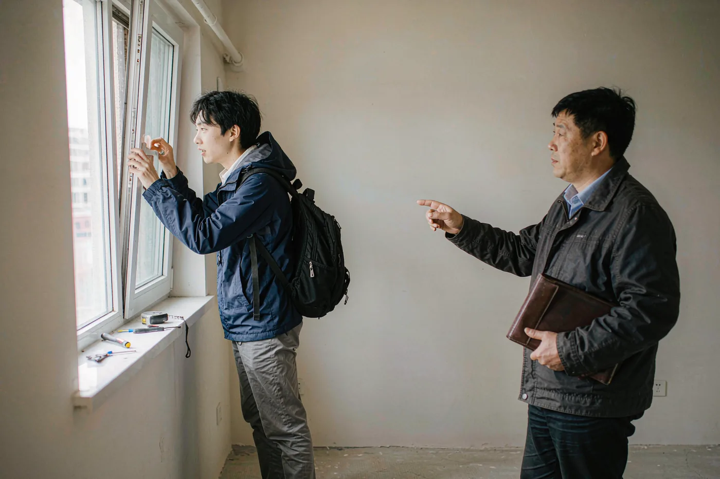 An international student checking the window of a rental apartment while a Chinese letting agent points out details