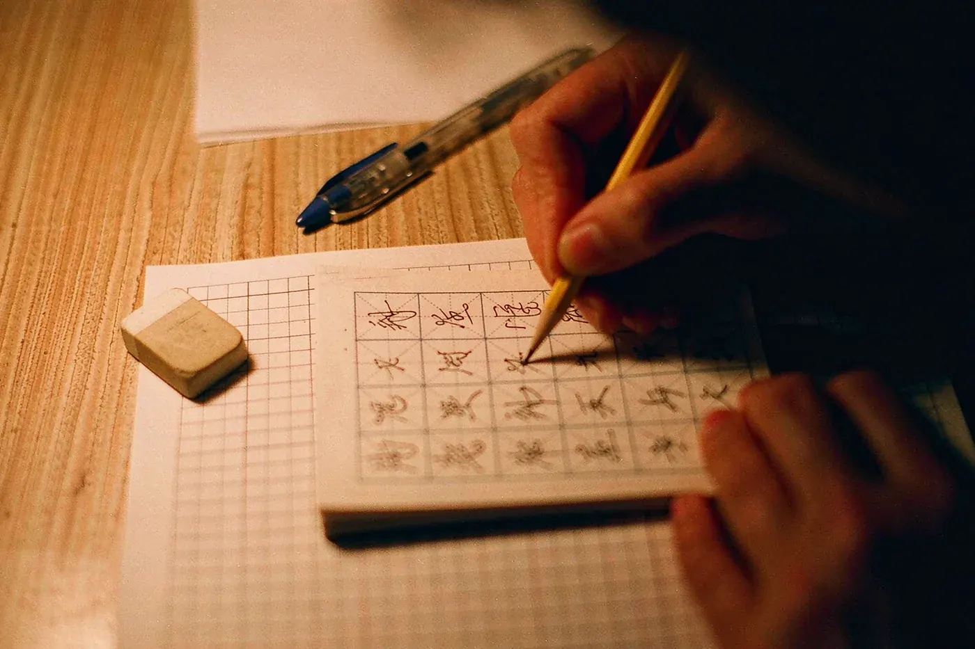 Practising writing Chinese characters in a gridded notebook on a desk