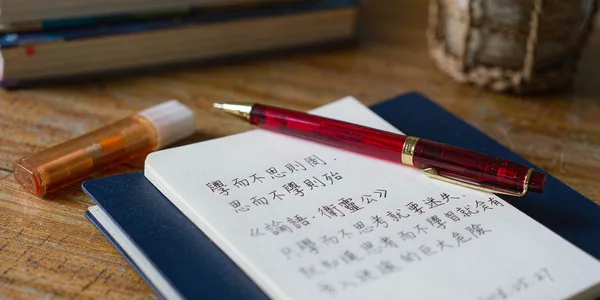 Close-up of a notebook with handwritten Chinese characters and a red pen
